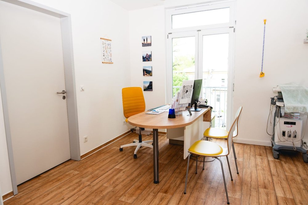 Helles Sprechzimmer mit Schreibtisch und großen Fenstern